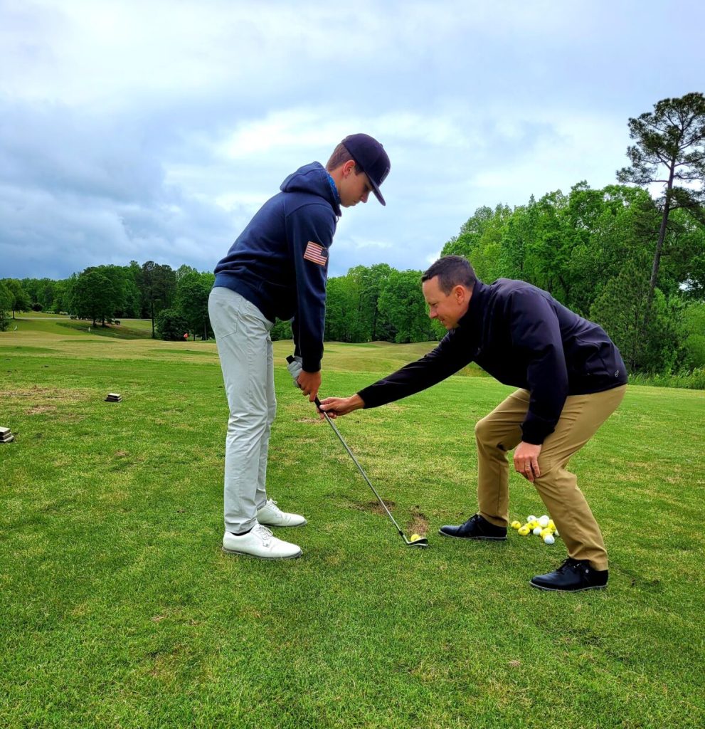 Instructor assisting young player with swing on golf course